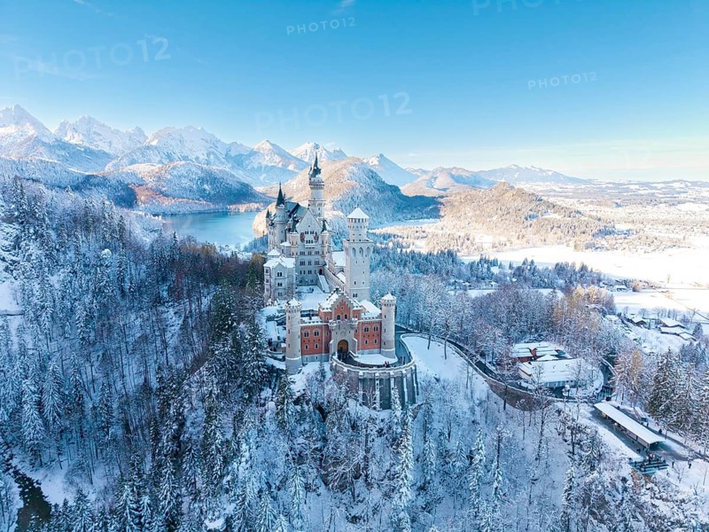 Wintery Neuschwanstein Castle with bright sky, surrounded by snow-capped mountains and forests, Schwangau near Füssen, Ostallgäu, Allgäu, Bavaria, Germany
