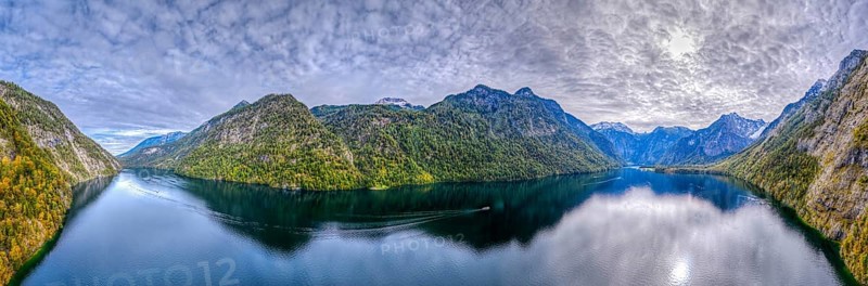 Calm lake with boat surrounded by high mountains and dramatic sky, Germany, Königssee, drone, panorama