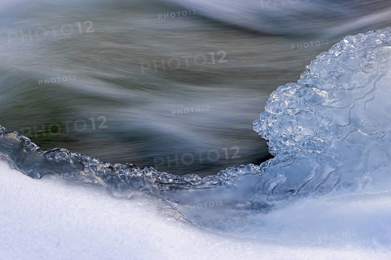 Ice formation formed by frost and freezing cold temperatures over running water of stream along riverbank / river bank in winter