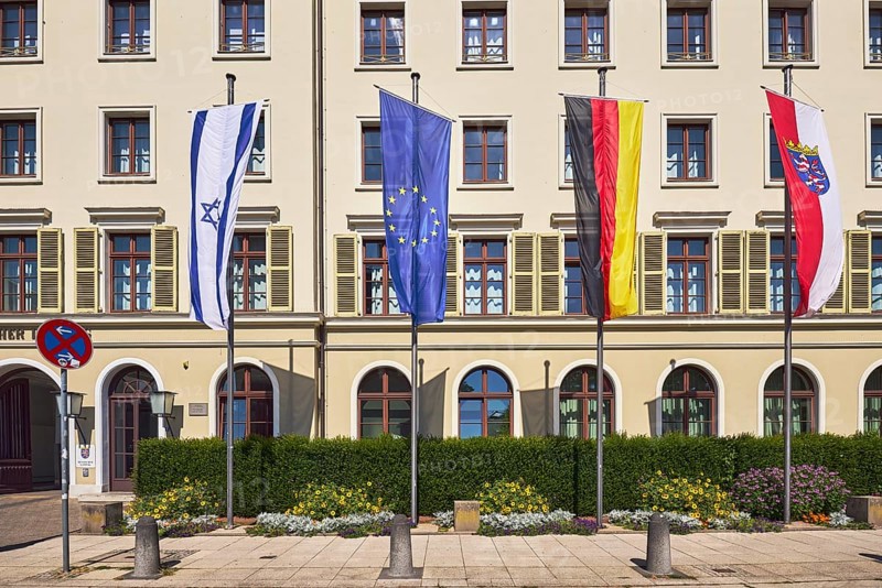 Flags, Israeli flag, German flag, European flag, flag of Hesse, flagpoles, state parliament, façade with windows and shutters, barrier bollard, sidewalk made of pavement tiles, hedge, flower bed, sunny, Schlossplatz, Wiesbaden, state capital, district-free city, Hesse, Germany