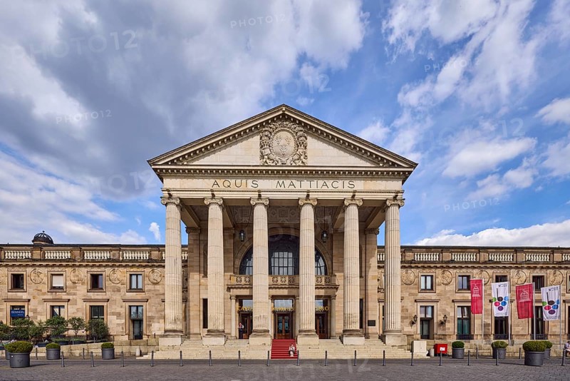 Spa hotel, neoclassical style with elements of Art Nouveau, architect Friedrich von Thiersch, inscription Aquis Mattiacis, pillars, advertising flag on flagpoles, street made of bricks, blue sky, cumulus clouds, Nimbostratus clouds, Kurhausplatz, Wiesbaden, state capital, district-free city, Hesse, Germany