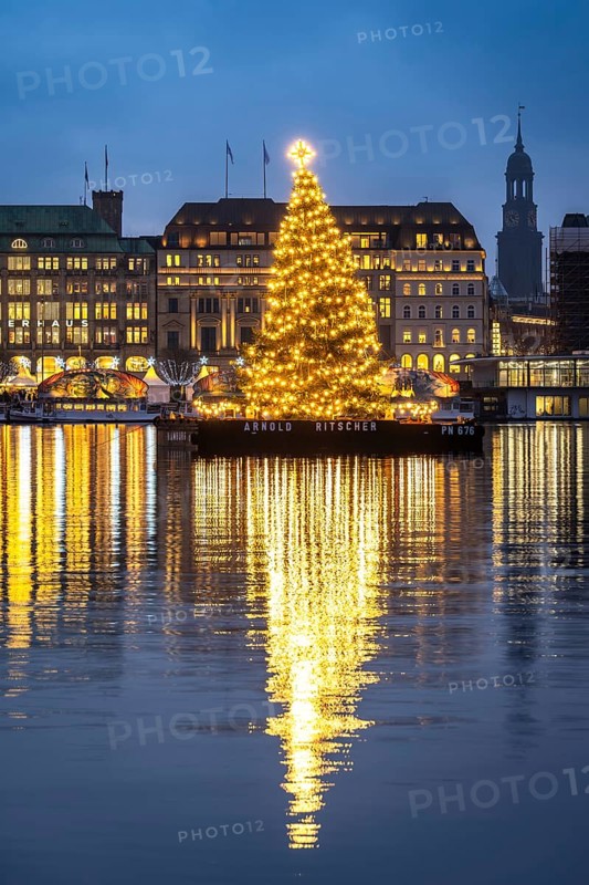 The decorated and illuminated Alster fir tree on the Inner Alster with reflections on the water in December at the blue hour with the main church of St. Michaelis, Jungfernstieg, Hamburg, Germany