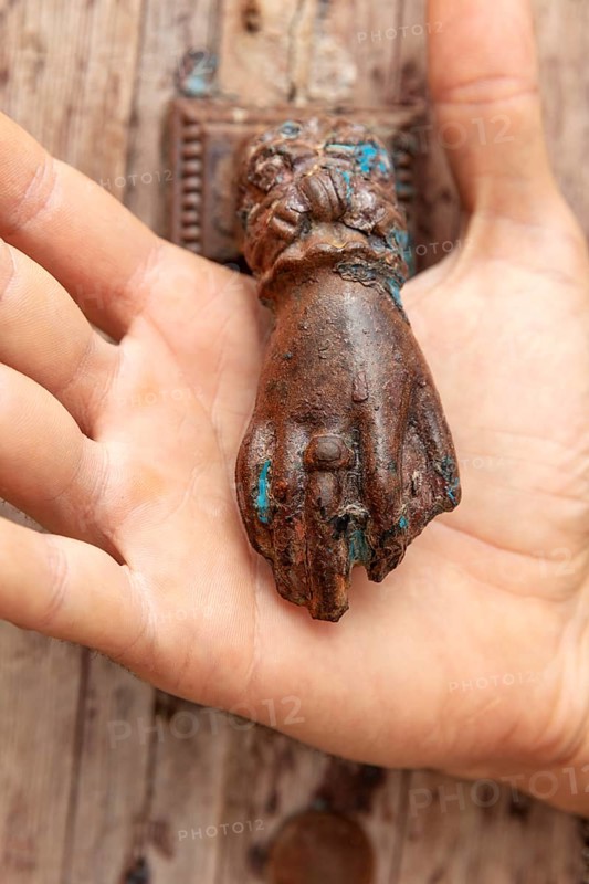 Rusty antique door knocker in the shape of a hand held by one hand