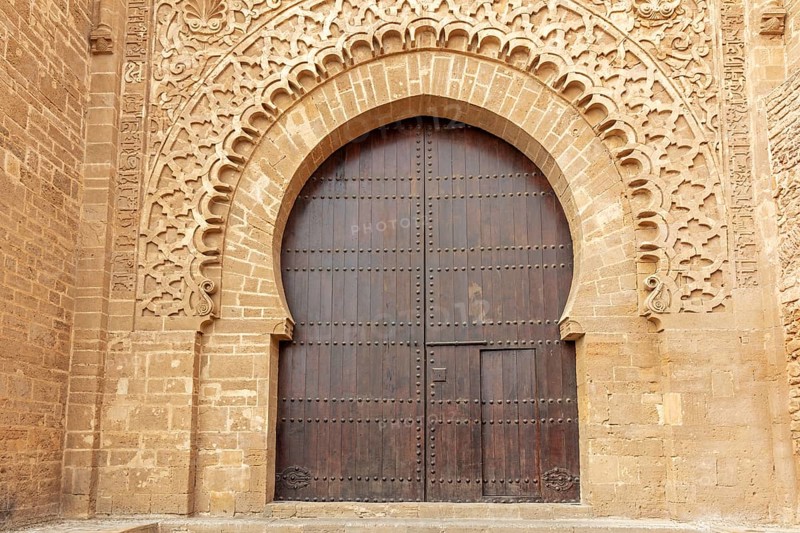 Large wooden gate with ornate stone carvings in an old wall