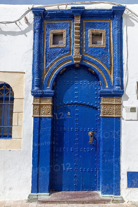 Blue, ornately decorated door in a white wall