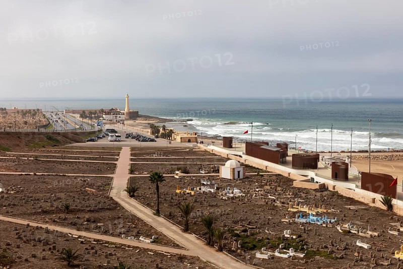 View of coast with cemetery and lighthouse, under cloudy sky