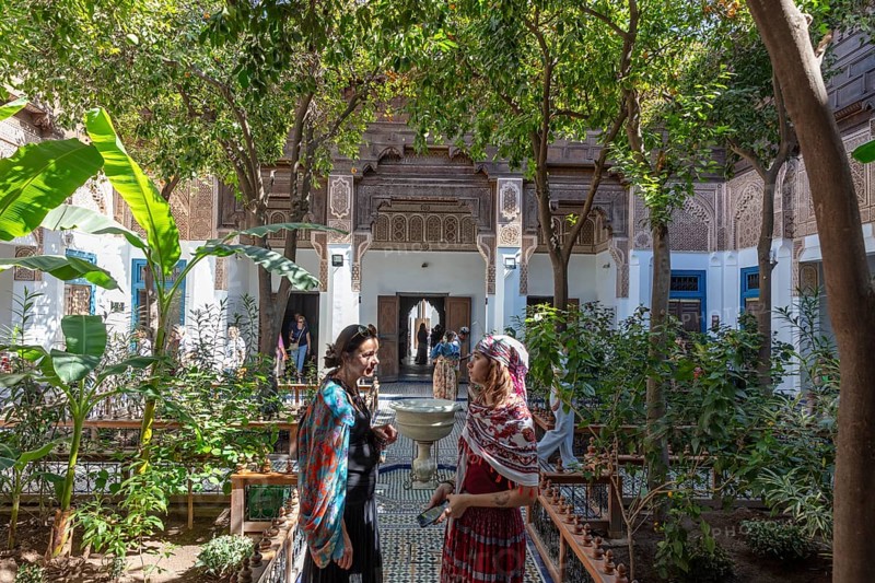 Two woman are talking in the green courtyard of the Bahia Palace with traditional architecture