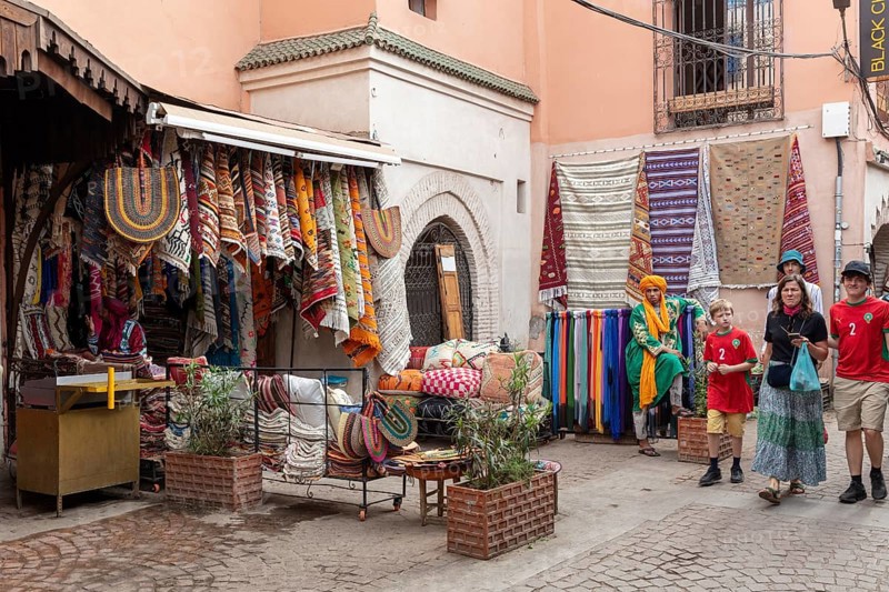Small street full of colorful textiles in a Moroccan bazaar surrounded by visitors
