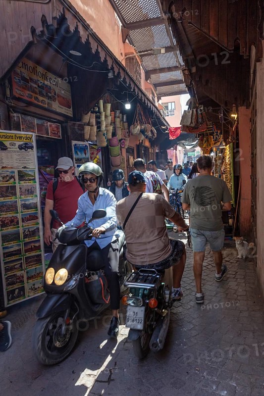 Lively market alleyway with people and scooters in traditional Moroccan style