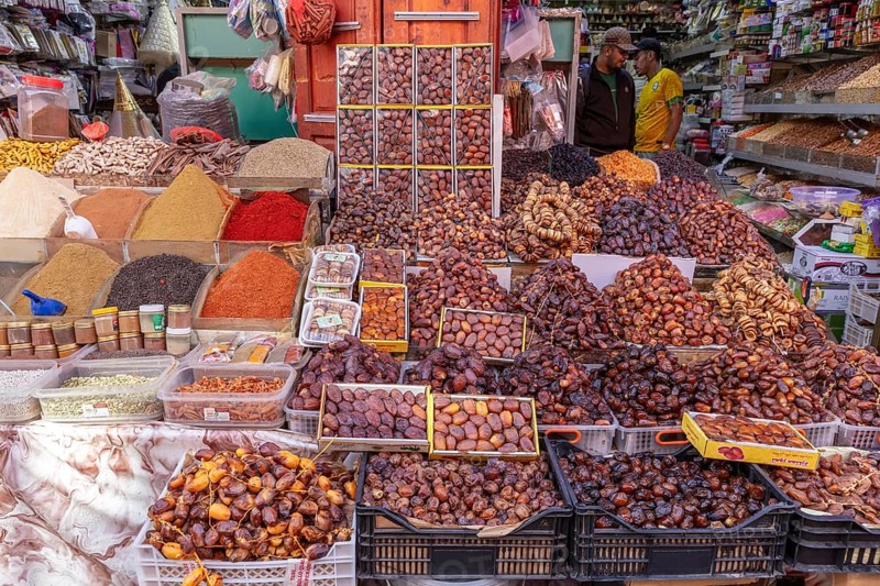 Market stand with a variety of spices and dates, surrounded by people