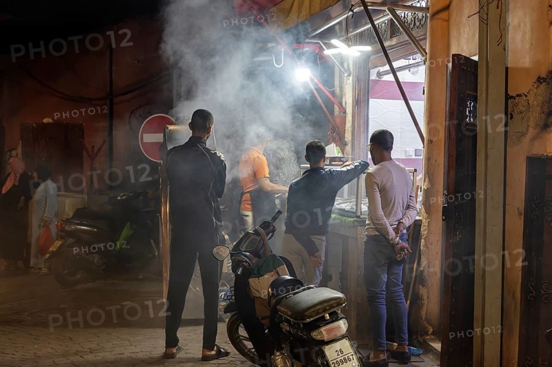 Nocturnal street scene with people, smoke from cooking areas and scooters in a busy area