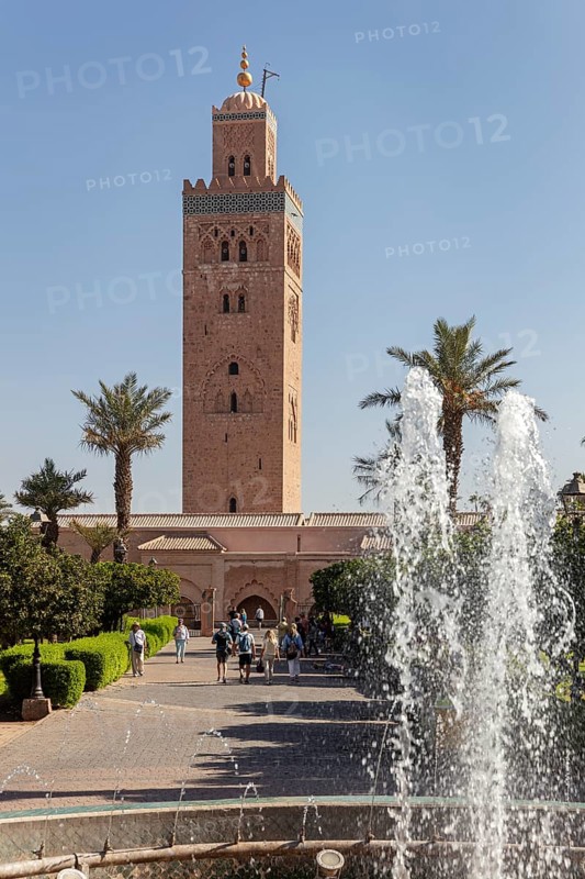 The Koutoubia Mosque in Marrakech, surrounded by palm trees and a sparkling fountain, visited by tourists