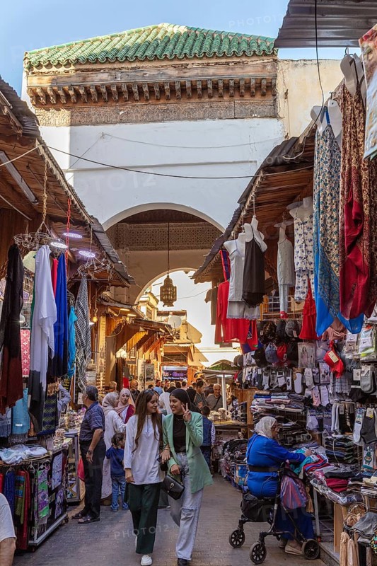Bustling market corridor with numerous clothes and fabrics under an archway
