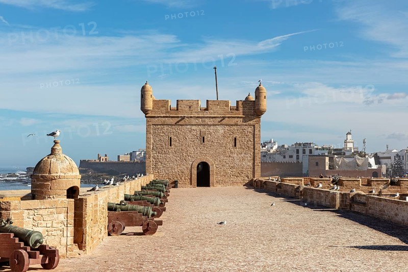 Historic fortress with cannons surrounded by a stone wall with a view of the sea under a blue sky