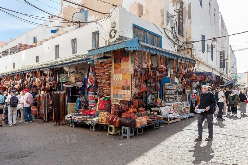 Bustling market with stalls selling leather goods and bags in a lively street scene