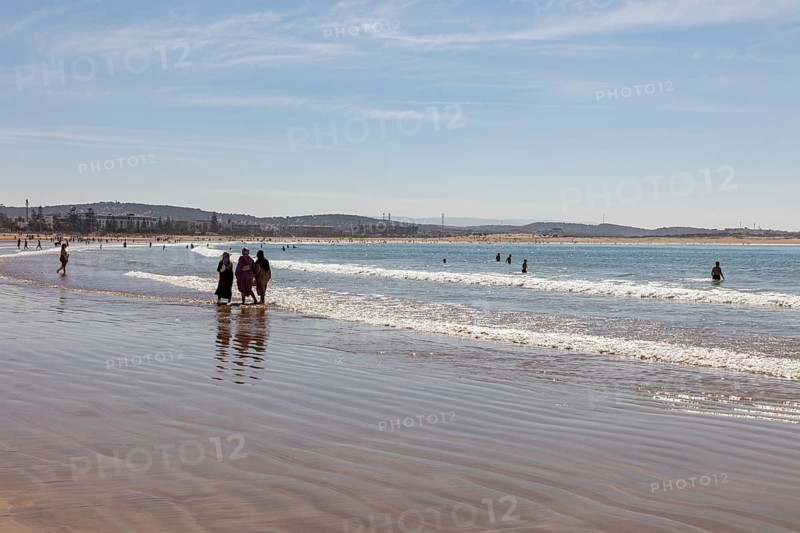 People walking on the beach in shallow water under clear sky