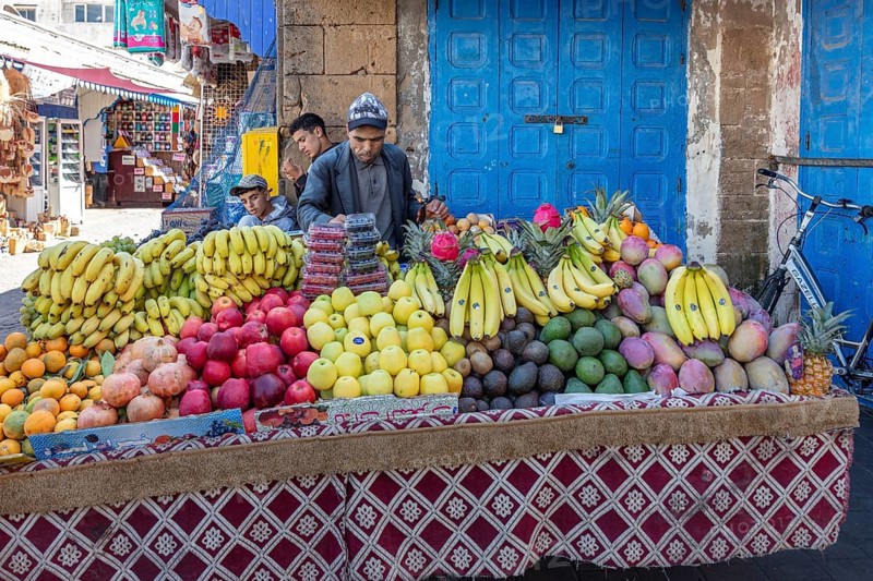 Well-stocked fruit stand with colorful fruits in front of a blue door