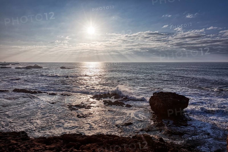 View of the sea at sunset with rocks and waves under a cloudy sky