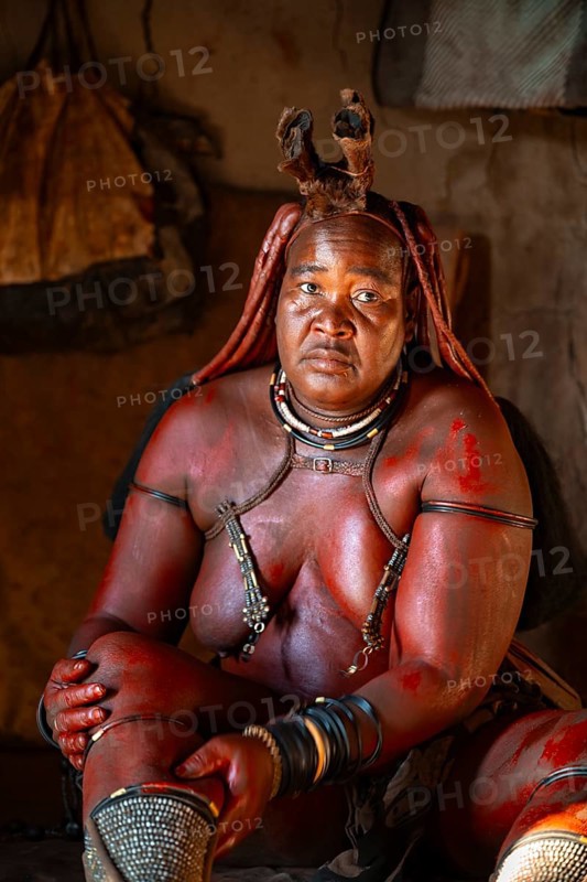 Elderly Himba woman rubbing herself with red paste for skin care, in a hut, traditional Himba village, Kaokoveld, Kunene, Namibia