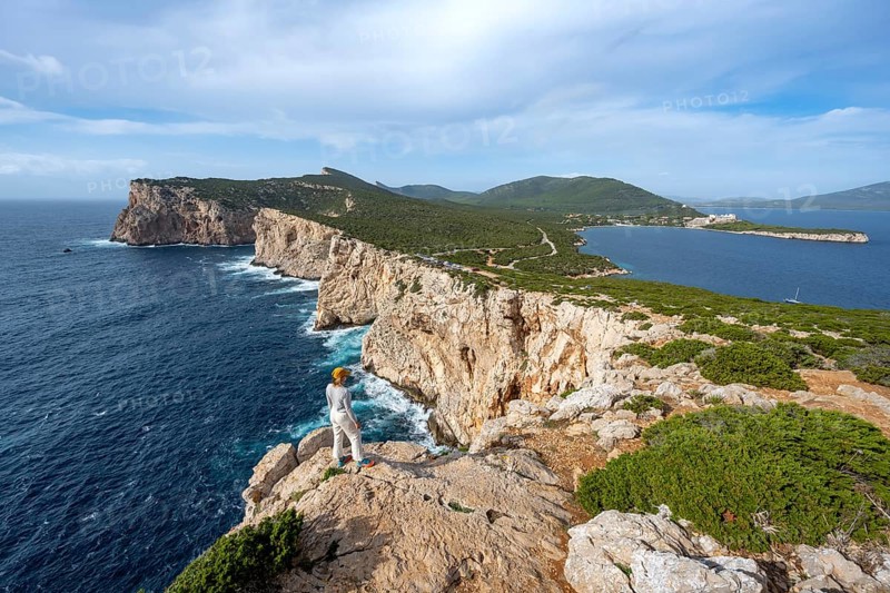 Tourist enjoying the view of steep cliffs by the sea, coastal landscape, cliffs on the Capo Caccia headland, Alghero, Sardinia, Italy
