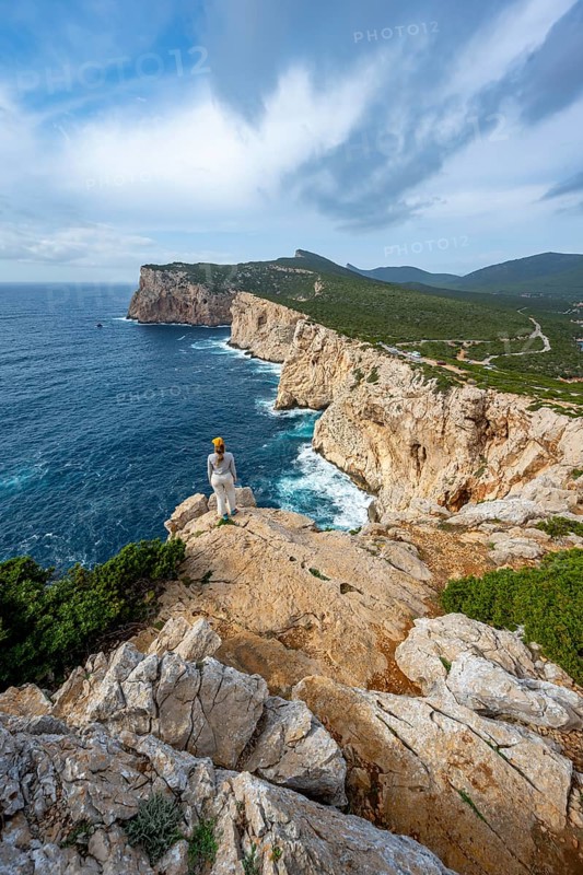Tourist enjoying the view of steep cliffs by the sea, coastal landscape, cliffs on the Capo Caccia headland, Alghero, Sardinia, Italy