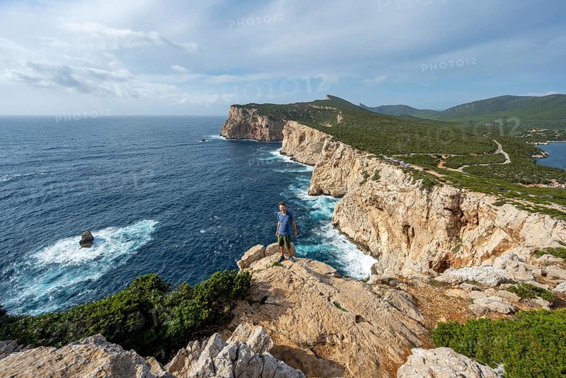Tourist enjoying the view of steep cliffs by the sea, coastal landscape, cliffs on the Capo Caccia headland, Alghero, Sardinia, Italy