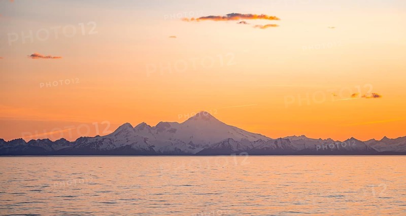 View of Cook Inlet on white mountain peaks of Mount Iliamna at sunset, picturesque golden light of the midnight sun, mountains of the Aleutian Range, Anchor Point, Anchor River State Recreation Area, Alaska, USA