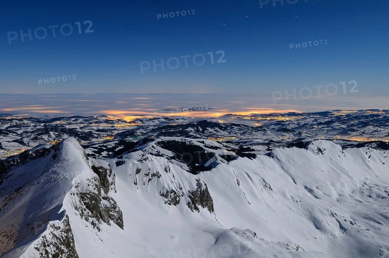 Night shot, long exposure of the 2506 meter high Säntis into the wintery, snow-covered, fog-covered foothills of the Alps illuminated by the villages, during a clear full moon night, Canton of Appenzell, Switzerland