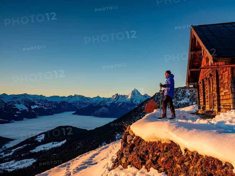 Mountaineers enjoy the sunrise in front of an alpine hut in winter, the Watzmann behind, fog in the valley, Berchtesgaden Alps, Scheibenkaser, Marktschellenberg, Berchtesgadener Land, Upper Bavaria, Bavaria, Germany