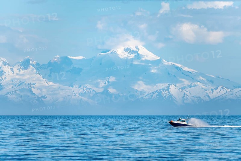 View over Cook Inlet to white mountain peaks of Mount Iliamna, motor boat rides on the ocean, mountains of the Aleutian Range, Anchor Point, Anchor River State Recreation Area, Alaska, USA