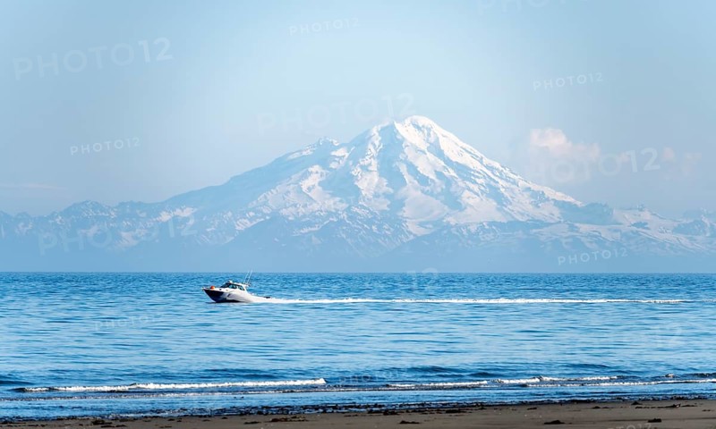 View over Cook Inlet to white mountain peaks of Mount Redoubt, motor boat rides on the ocean, Aleutian Mountains, Anchor Point, Anchor River State Recreation Area, Alaska, USA