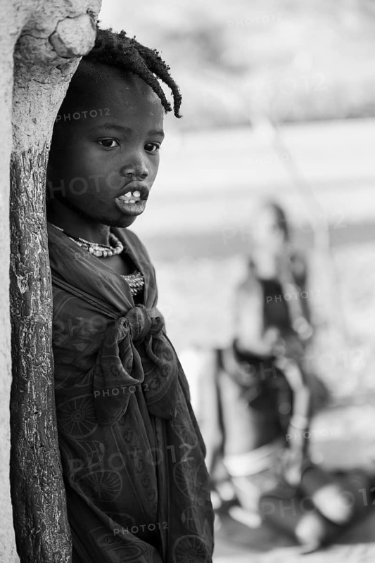 Black and white, Himba girl leaning at a traditional clay hut, in the morning, traditional Himba village, Kaokoveld, Kunene, Namibia