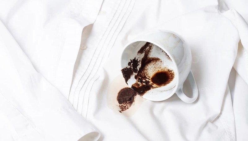 A white cup with the remains of coffee, spilled, lies on a white shirt, there are no people, a soft focus