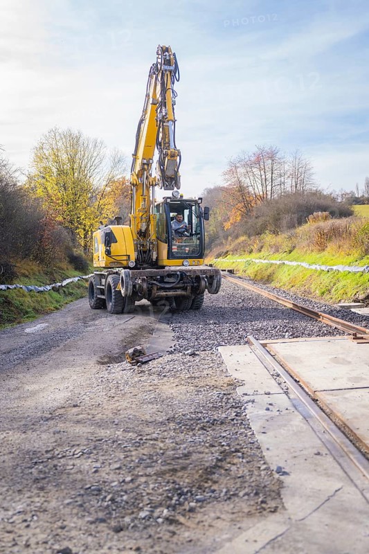 Yellow excavator lays tracks in autumn landscape, preparation of track work, track construction of the Hermann Hesse Railway, Calw, Germany