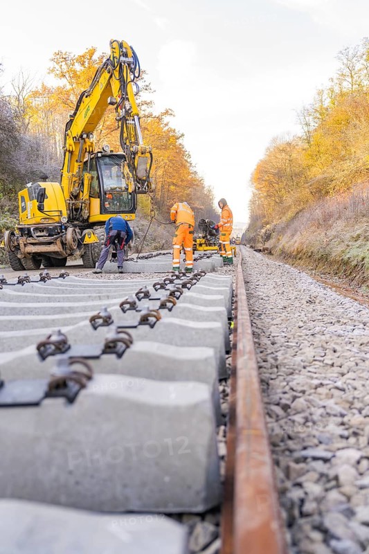 Workers lay concrete ties along an autumnal railway line with the help of an excavator, Hermann Hesse Railway track construction, Calw, Germany