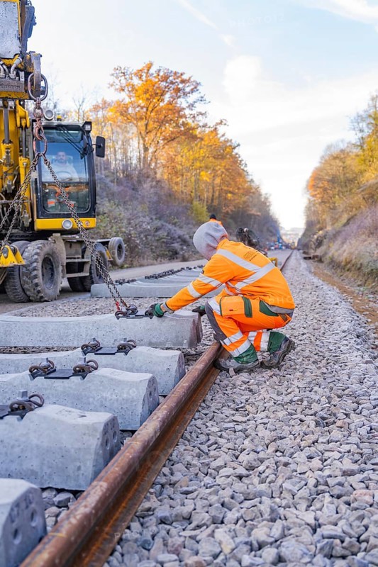Workers lay concrete ties along a long railway line in an autumn landscape, track construction of the Hermann Hesse Railway, Calw, Germany