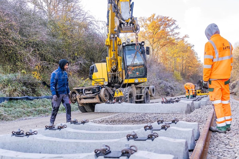 Track construction with a yellow excavator, where workers lay heavy concrete ties, Hermann Hesse Railway track construction, Calw, Germany