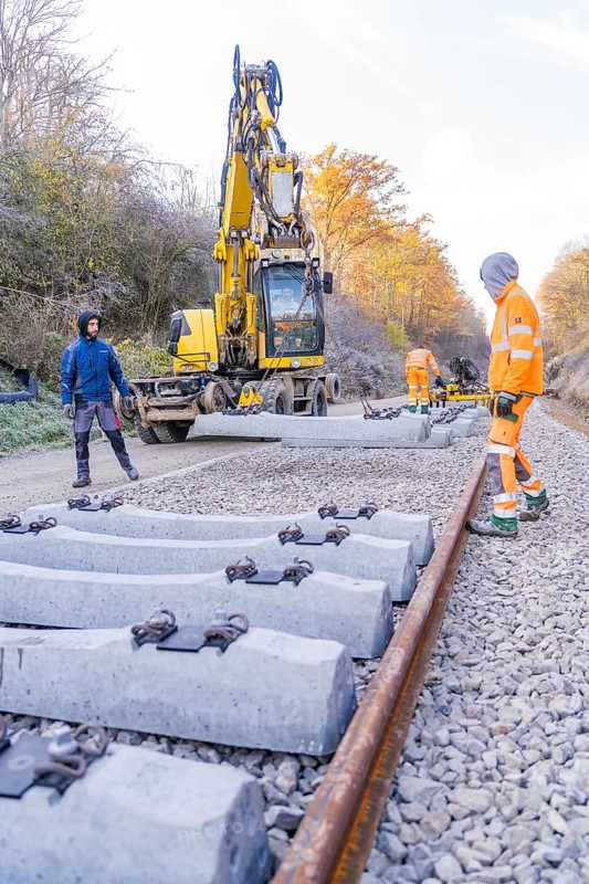 Construction workers lay concrete ties with a yellow excavator on a railway line in autumn, track construction of the Hermann Hesse Railway, Calw, Germany