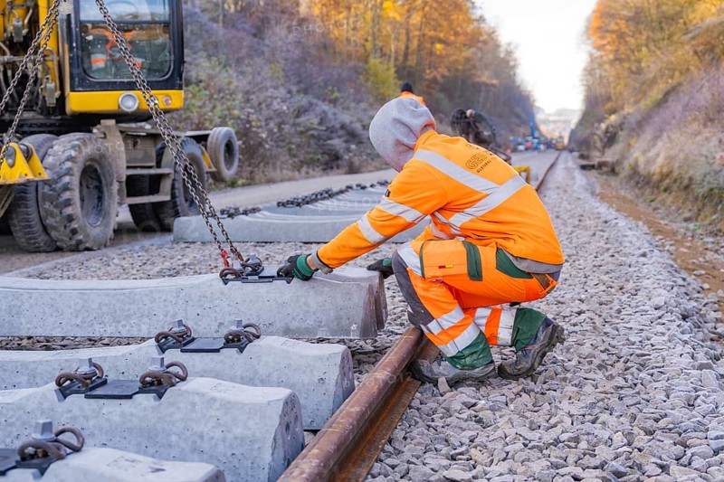 A construction worker wearing glowing safety clothing works on sleepers along the railway line, Hermann Hesse Railway track construction, Calw, Germany