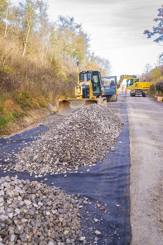 Construction site with construction machinery and piles of gravel next to an asphalted road, Hermann Hesse Railway track construction, Calw, Germany