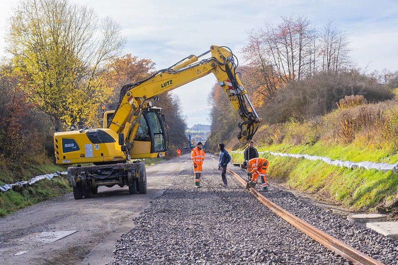 Yellow excavator on a construction site in autumn, workers laying tracks on gravel, Hermann Hesse Railway track construction, Calw, Germany