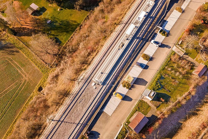 View from above of a train station with an adjacent street and autumnal greenery in the area, new Hermann Hessebahn station, Ostelsheim, Calw district, Germany