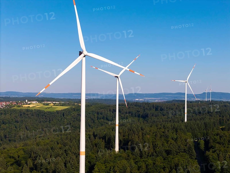 Three wind turbines rise above a green forest under a clear sky, near Schorndorf, Remstal, Baden-Württemberg, Germany
