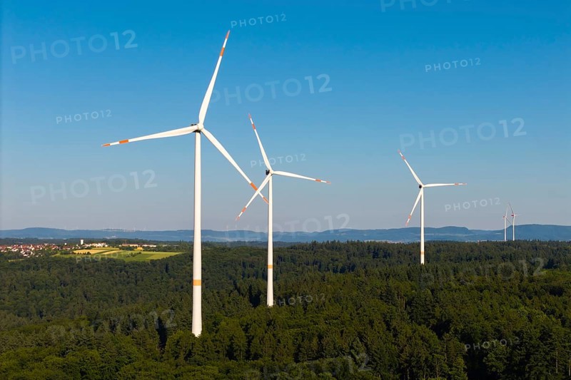 Wind turbines stand in a wooded landscape under a wide blue sky, near Schorndorf, Remstal, Baden-Württemberg, Germany