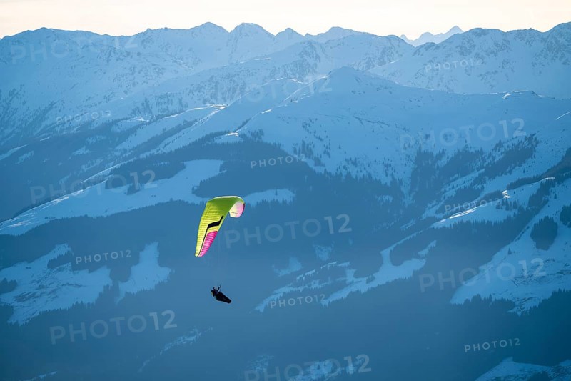 Paragliders flying over snowy mountain peaks in winter in evening light, Kitzbühel Alps, Tyrol, Austria