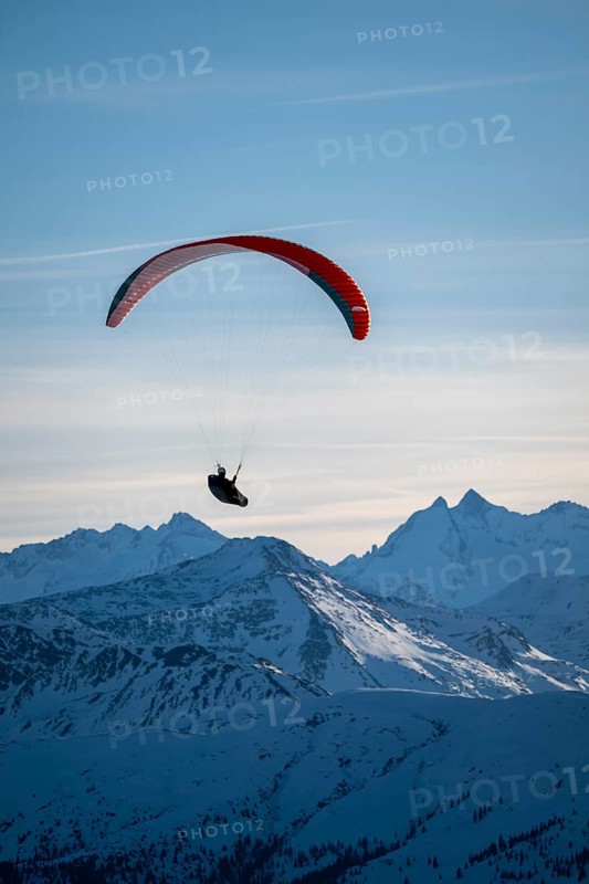 Paragliders flying over snowy mountain peaks in winter in evening light, Kitzbühel Alps, Tyrol, Austria