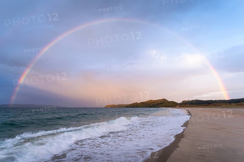 Landscape with sea and sandy beach in New Zealand with rainbow, in the evening at golden hour. Otama Beach, Coromandel Peninsula, Waikato, New Zealand