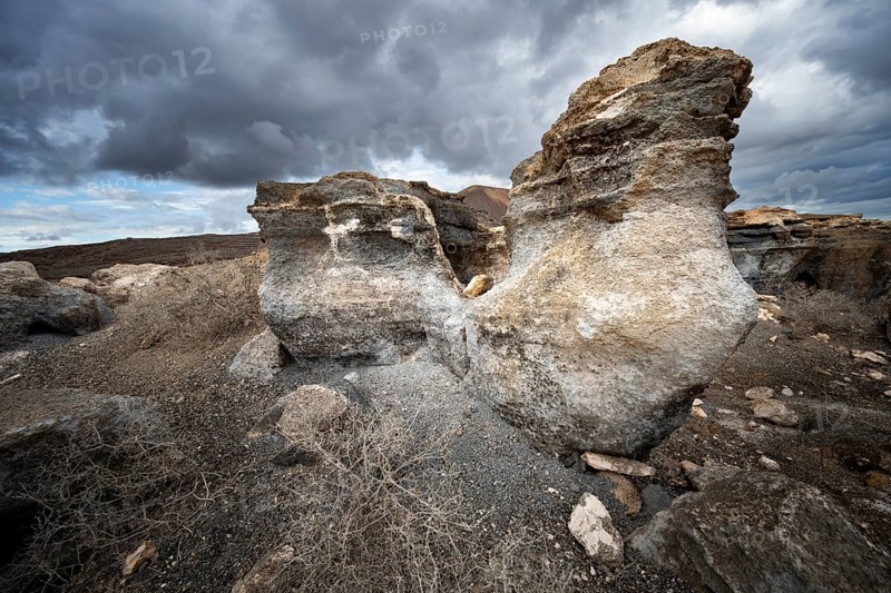Eroded rock formations in volcanic landscape with dramatic cloudy skies, Ciudad Estratificada or Los Roferos, Antigua Rofera de Teseguite, Lanzarote, Canary Islands, Spain