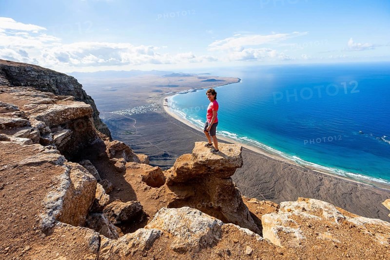 Woman enjoying the view from the Risco de Famara cliffs on Famara beach, Playa de Famara with La Calaeta, Lanzarote, Canary Islands, Spain