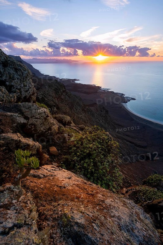 View from steep cliffs to sea and coast with sun stars, Mirador del Porrito viewpoint at sunset, Lanzarote, Canary Islands, Spain